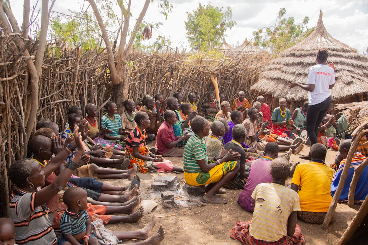 A gathering of people in traditional African village, sitting and interacting outdoors.